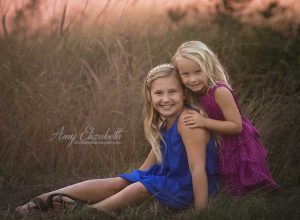 sisters sitting by tall grasses and pink sky