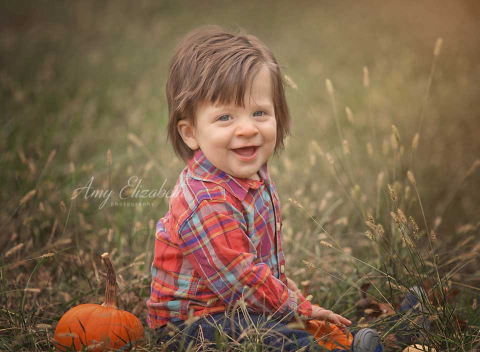 baby boy wearing plaid sitting with pumpkins