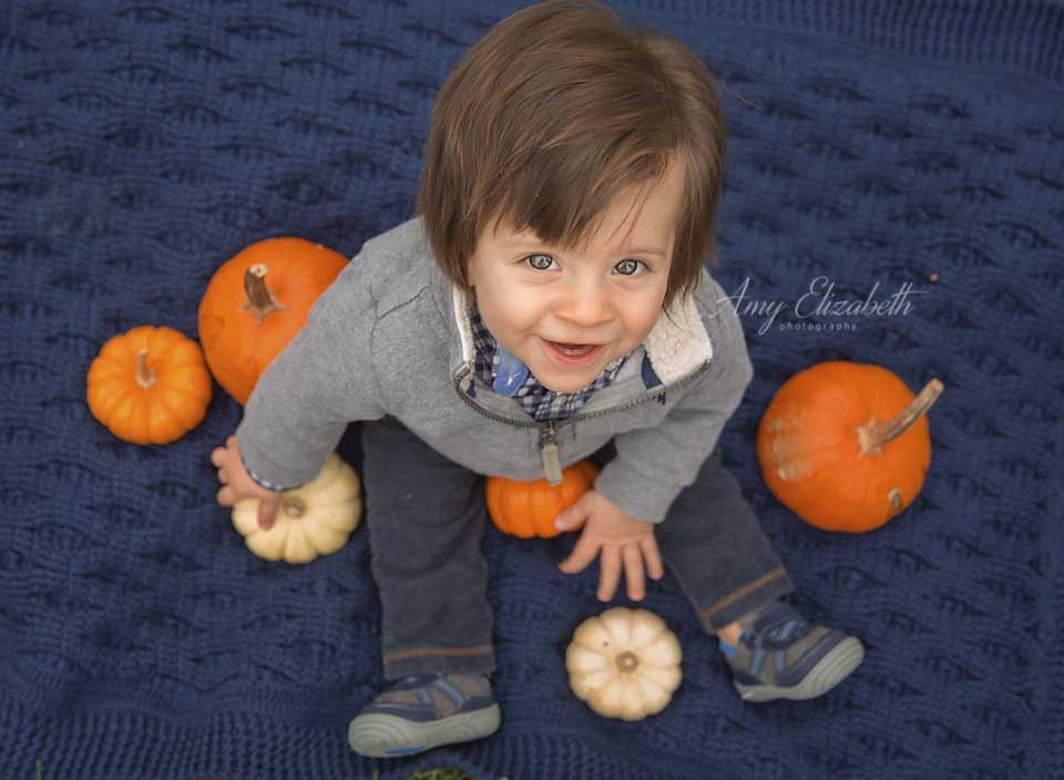 baby boy looking up from pumpkins 